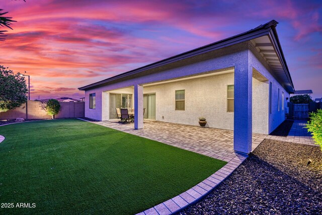 back house at dusk with a patio area and a yard