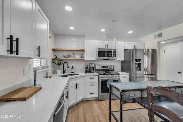 kitchen with sink, light stone counters, white cabinetry, and appliances with stainless steel finishes