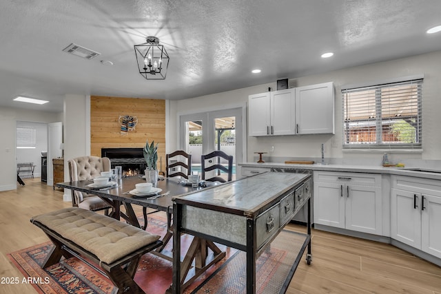 kitchen featuring a textured ceiling, light wood-type flooring, white cabinetry, and a large fireplace