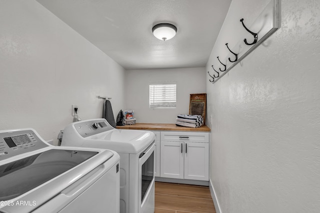 laundry room featuring washing machine and clothes dryer, a textured ceiling, light hardwood / wood-style floors, and cabinets