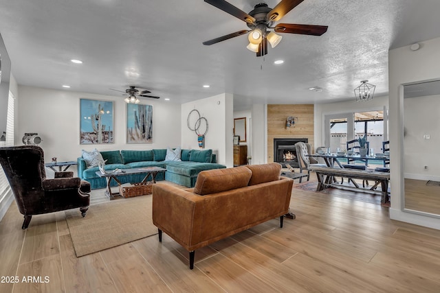 living room with ceiling fan, a large fireplace, a textured ceiling, and light wood-type flooring