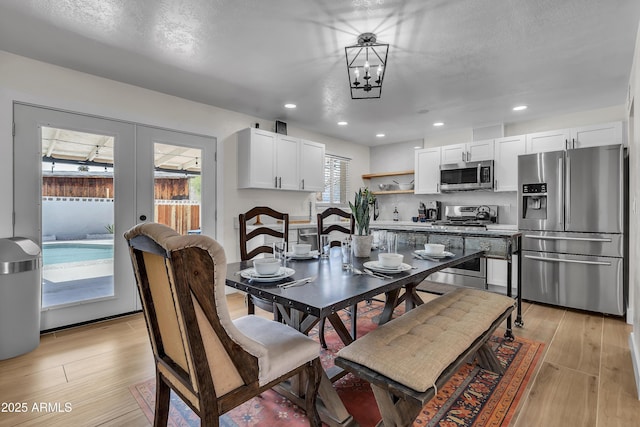 dining area featuring a textured ceiling, light hardwood / wood-style flooring, french doors, and an inviting chandelier