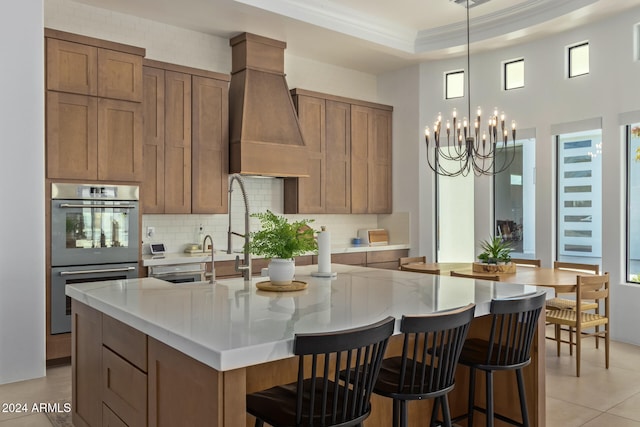 kitchen with an inviting chandelier, hanging light fixtures, tasteful backsplash, an island with sink, and stainless steel double oven