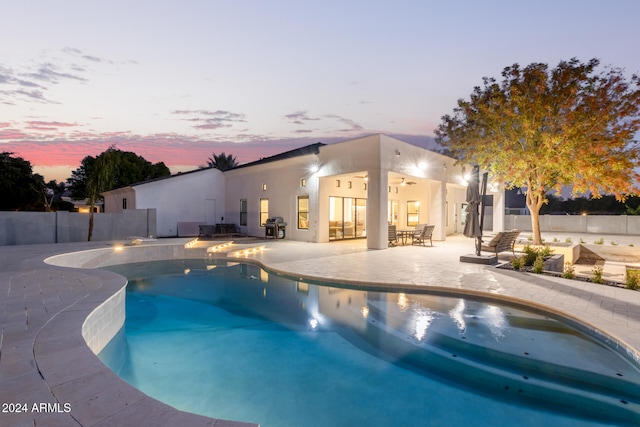 pool at dusk with a patio area and grilling area