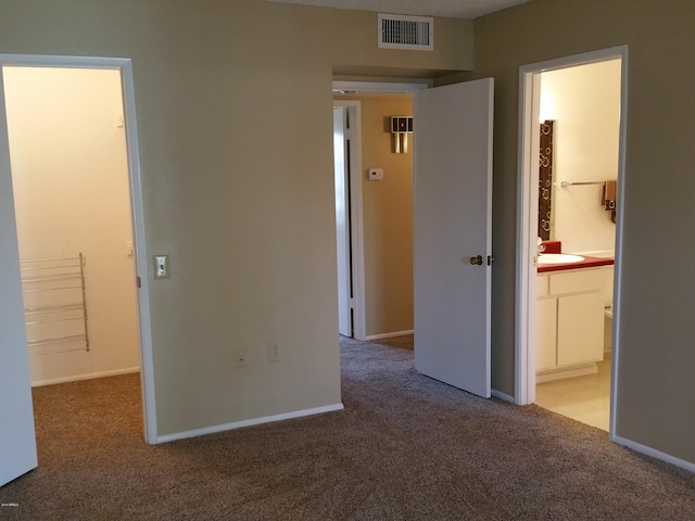 unfurnished bedroom with ensuite bathroom, sink, carpet floors, and a spacious closet