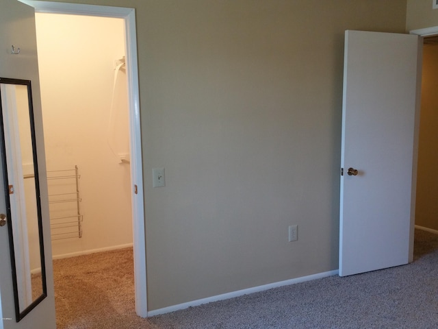 unfurnished bedroom with a walk in closet, a closet, and light colored carpet