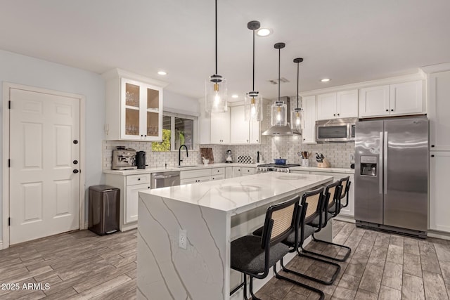 kitchen featuring sink, a kitchen island, pendant lighting, stainless steel appliances, and wall chimney range hood