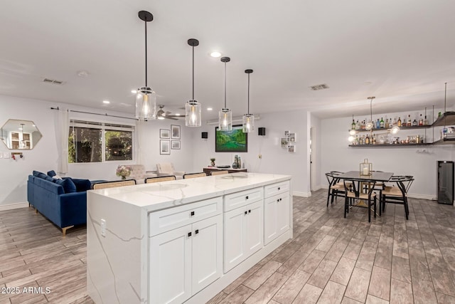 kitchen featuring white cabinetry, pendant lighting, light stone countertops, and a center island