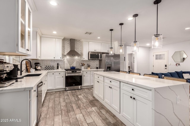 kitchen featuring white cabinetry, a center island, hanging light fixtures, stainless steel appliances, and wall chimney range hood