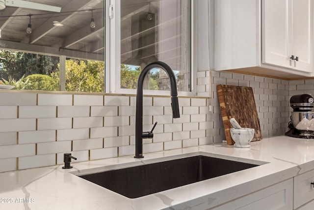 details with light stone counters, sink, tasteful backsplash, and white cabinets