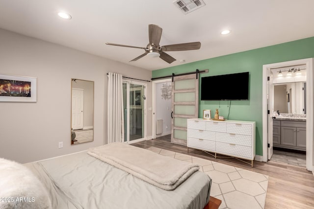 bedroom with connected bathroom, access to exterior, ceiling fan, a barn door, and light hardwood / wood-style floors