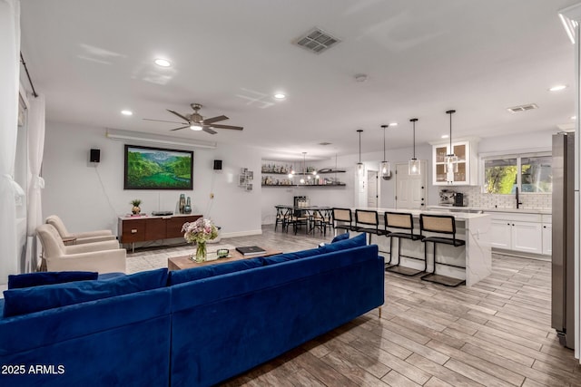 living room featuring ceiling fan, sink, and light hardwood / wood-style floors