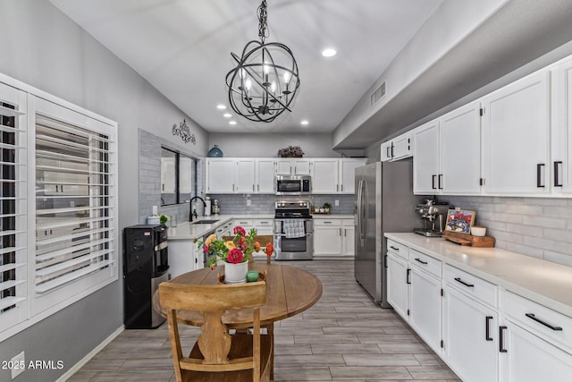 1231 W Mediterranean Dr, Gilbert, AZ 85233 - kitchen featuring stainless steel appliances, a sink, tasteful backsplash, white cabinetry, and a chandelier