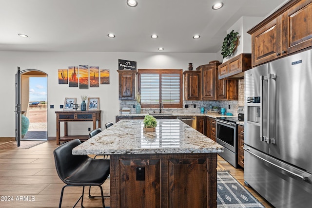 kitchen featuring tasteful backsplash, stainless steel appliances, light stone counters, a kitchen island, and light hardwood / wood-style floors