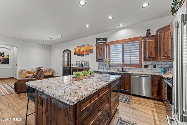 kitchen with tasteful backsplash, stainless steel appliances, light wood-type flooring, sink, and a kitchen island