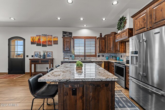 kitchen with refrigerator, a center island, backsplash, light stone countertops, and stove