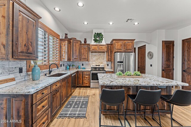 kitchen featuring appliances with stainless steel finishes, tasteful backsplash, sink, light hardwood / wood-style floors, and a kitchen island