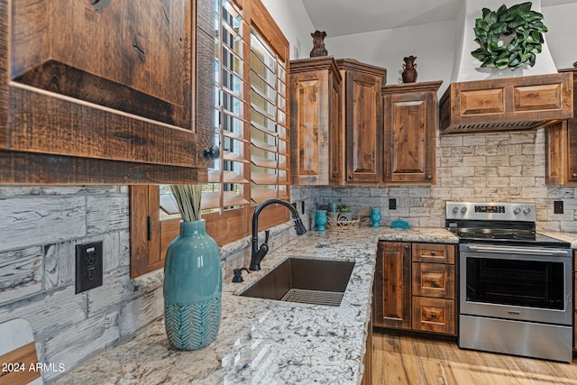 kitchen with light wood-type flooring, light stone counters, sink, and stainless steel range with electric stovetop