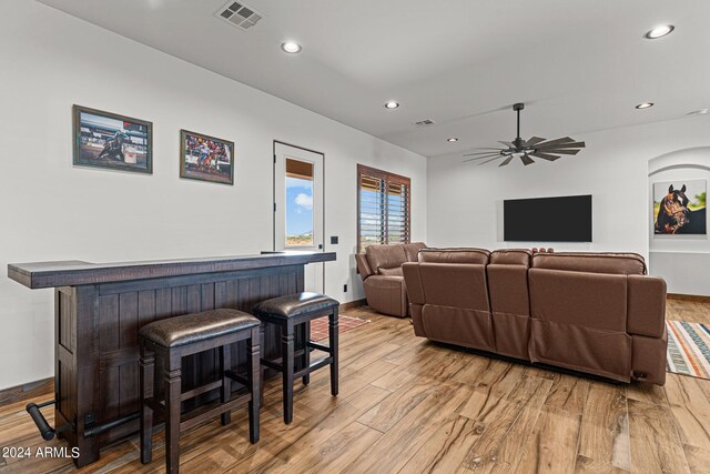 living room featuring light wood-type flooring, ceiling fan, and bar area