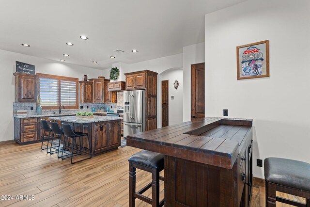 kitchen with light hardwood / wood-style floors, high end refrigerator, tasteful backsplash, and a kitchen breakfast bar