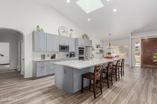 kitchen featuring gray cabinetry, hanging light fixtures, a large island with sink, stainless steel appliances, and decorative backsplash