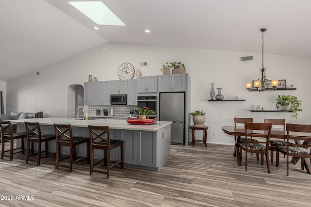 kitchen featuring decorative light fixtures, appliances with stainless steel finishes, a kitchen breakfast bar, gray cabinets, and decorative backsplash