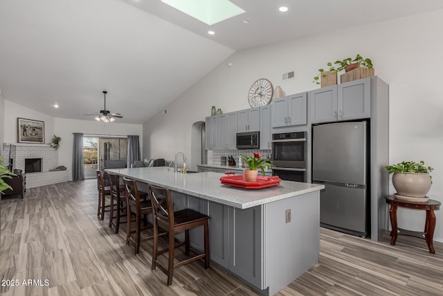 kitchen with gray cabinetry, tasteful backsplash, a skylight, stainless steel appliances, and a kitchen island with sink