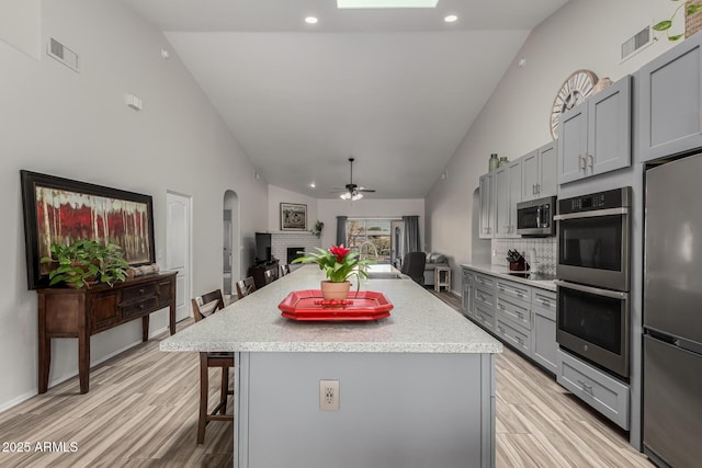 kitchen featuring appliances with stainless steel finishes, gray cabinetry, a kitchen breakfast bar, tasteful backsplash, and a kitchen island