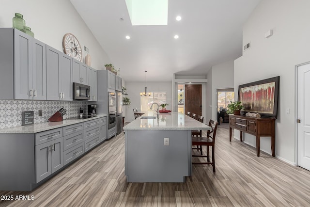 kitchen with appliances with stainless steel finishes, sink, a kitchen island with sink, and gray cabinetry