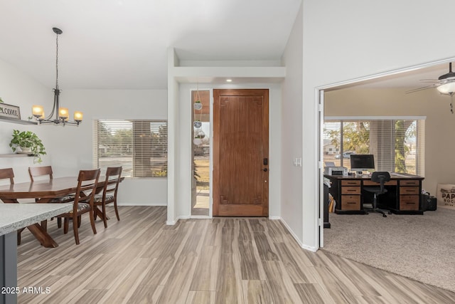 foyer with lofted ceiling, ceiling fan with notable chandelier, and light wood-type flooring