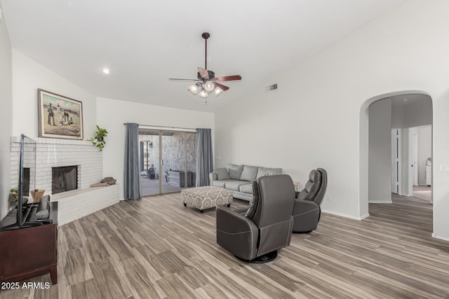 living room with wood-type flooring, lofted ceiling, ceiling fan, and a fireplace