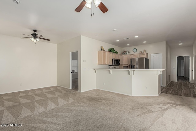 kitchen featuring stainless steel appliances, ceiling fan, light carpet, and a kitchen bar