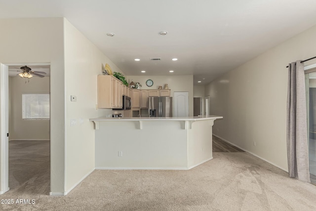 kitchen with light brown cabinetry, a breakfast bar area, ceiling fan, stainless steel appliances, and light carpet