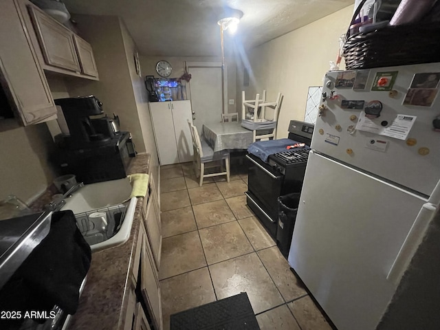 kitchen with light tile patterned flooring, a sink, light countertops, black range with gas stovetop, and freestanding refrigerator