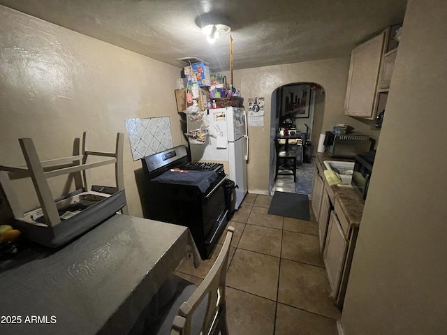 kitchen with arched walkways, gas range oven, freestanding refrigerator, light brown cabinets, and tile patterned floors