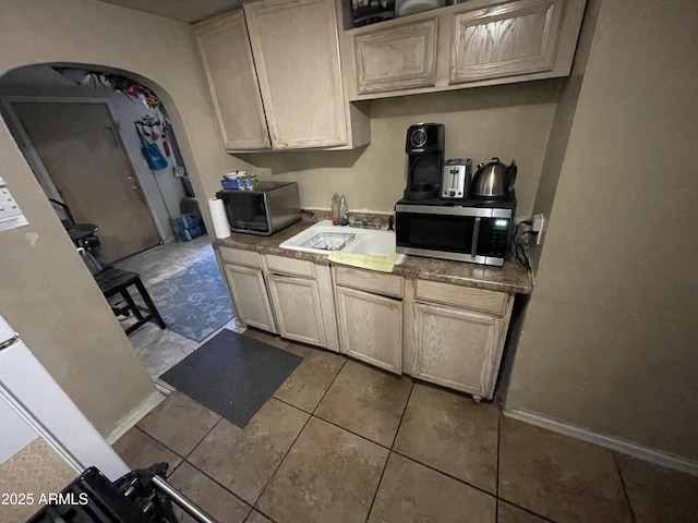 kitchen featuring arched walkways, stainless steel microwave, a sink, and baseboards