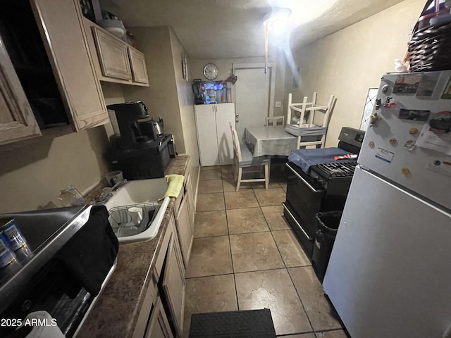 kitchen featuring light tile patterned floors, black gas range, a sink, and freestanding refrigerator