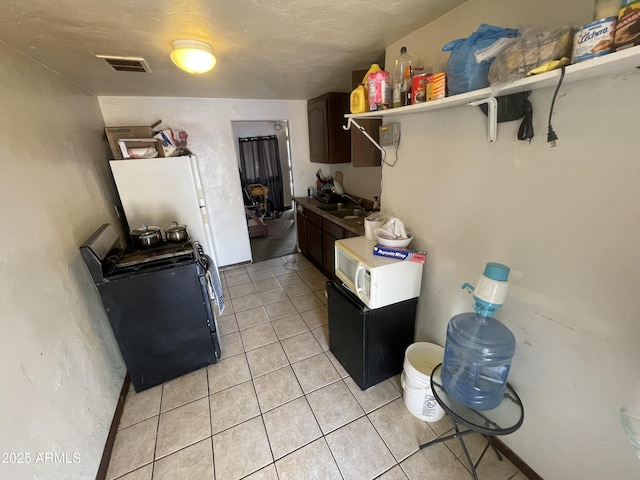 kitchen featuring visible vents, white microwave, stove, a sink, and light tile patterned flooring