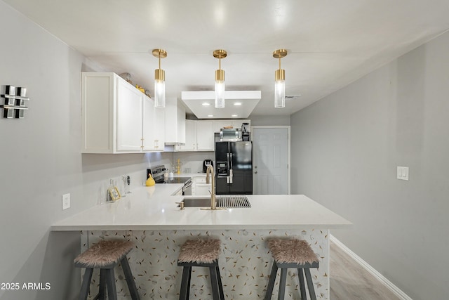 kitchen with stainless steel electric stove, light countertops, black fridge with ice dispenser, a peninsula, and a kitchen bar