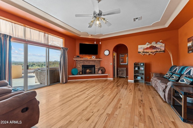 living room featuring a fireplace, light hardwood / wood-style floors, a tray ceiling, and ceiling fan