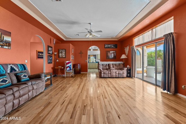 living room with ceiling fan, light hardwood / wood-style floors, and a raised ceiling