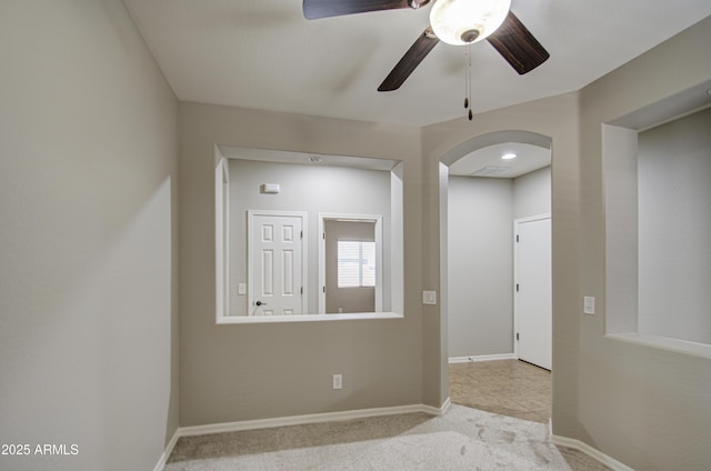 spare room with arched walkways, carpet flooring, a ceiling fan, and baseboards