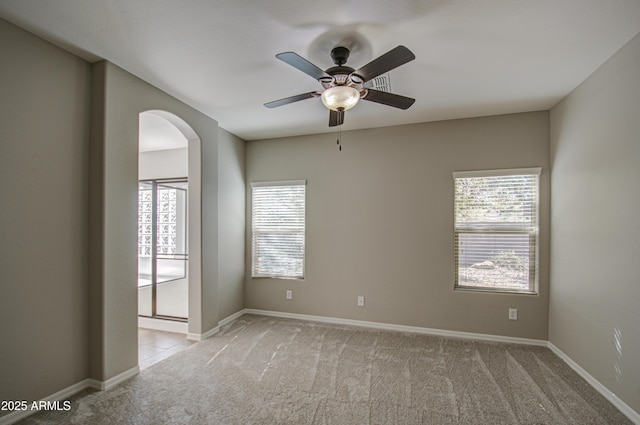 unfurnished room with baseboards, arched walkways, a ceiling fan, and light colored carpet