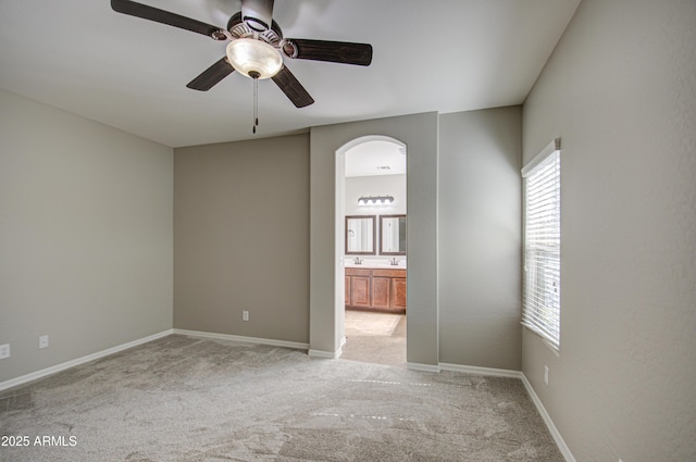 unfurnished room featuring light carpet, baseboards, arched walkways, and a ceiling fan