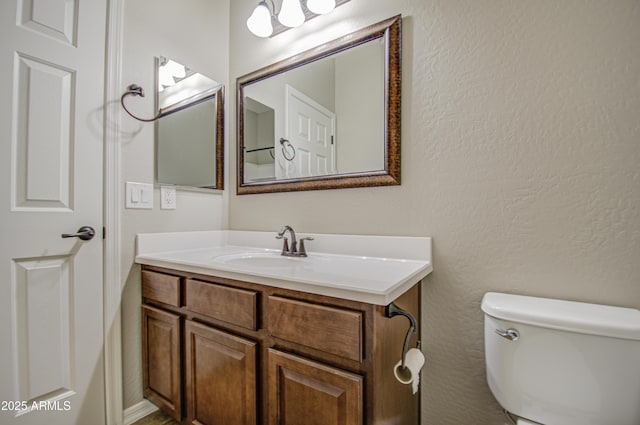 half bath featuring toilet, a textured wall, and vanity