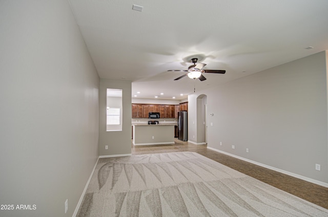 unfurnished living room with arched walkways, recessed lighting, light colored carpet, a ceiling fan, and baseboards