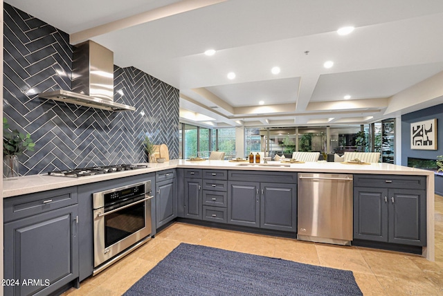 kitchen with gray cabinets, a sink, stainless steel appliances, wall chimney exhaust hood, and light countertops