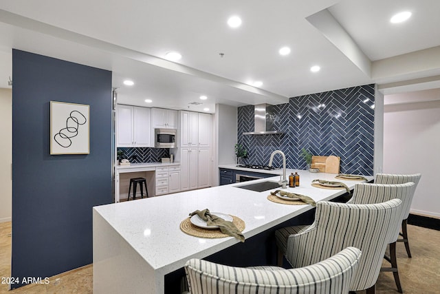 kitchen with stainless steel microwave, backsplash, a peninsula, wall chimney exhaust hood, and an accent wall