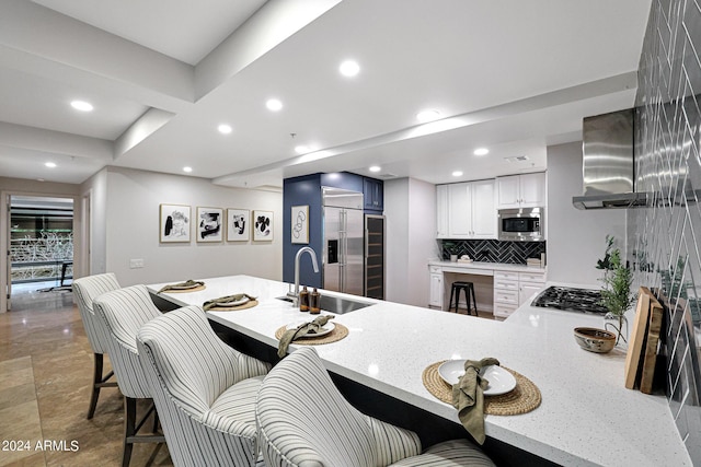 kitchen with light stone countertops, a peninsula, a sink, decorative backsplash, and built in appliances