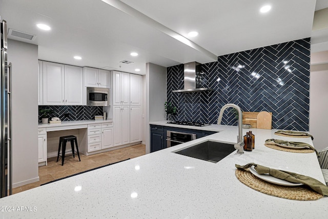 kitchen featuring light stone counters, stainless steel appliances, wall chimney exhaust hood, and a sink